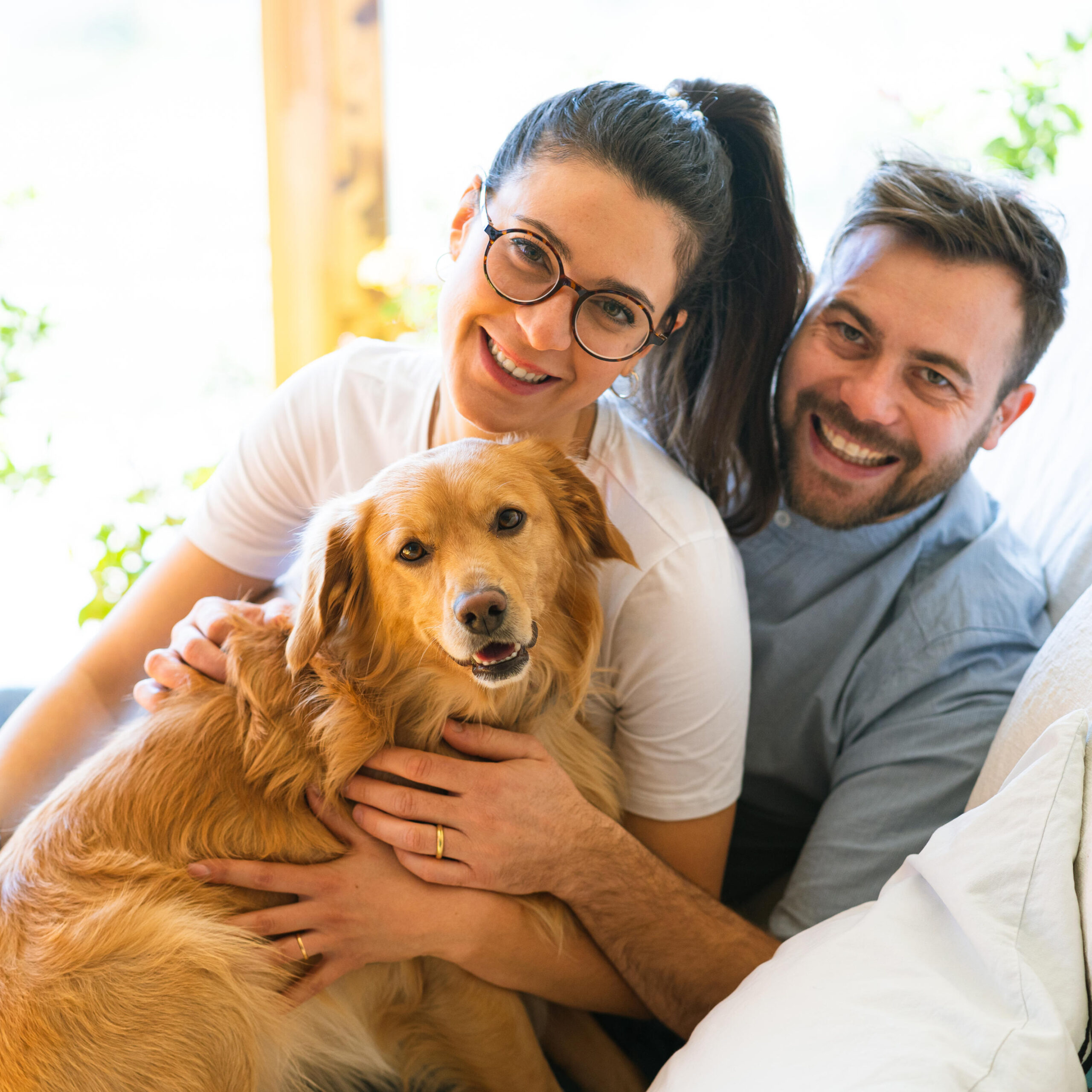 Happy couple with a golden retriever dog sitting on a sofa smiling and positive